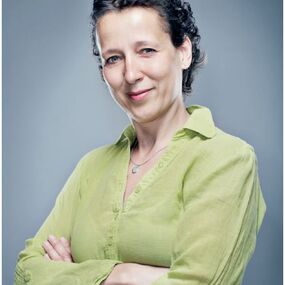 Frau in grüner Bluse lächelt zufrieden, wirbt für gutes Hören mit Kronemann Hörakustik.